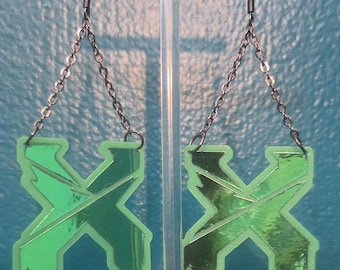 May include: A pair of dangling earrings featuring a bright neon green X-shaped pendant with a reflective metallic green centre. The pendants are suspended from dark metal chains and ear hooks, creating a sharp, angular design with a glossy finish.