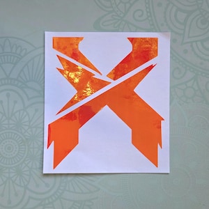 Peut inclure: Un autocollant carré blanc présentant une lettre X stylisée d'une couleur orange vive. Le motif possède une finition brillante et réfléchissante avec un aspect métallique texturé qui crée des reflets lumineux sur la surface de la lettre.