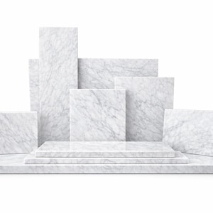May include: A collection of white marble display blocks and platforms. The arrangement includes rectangular and square shapes of varying sizes, creating a tiered and architectural presentation. The marble has a natural veining pattern.