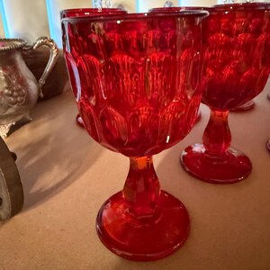 May include: Set of red vintage goblets. The ruby red glasses have a textured pattern on the bowl and a stem with a round base. The goblets are made of glass and are suitable for serving beverages. The glassware is a vintage style.