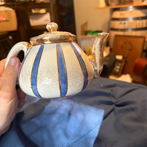 May include: A small, vintage teapot with a white base and vertical blue stripes. The lid, spout, and handle are accented with gold trim. The teapot is a classic design, perfect for serving tea.