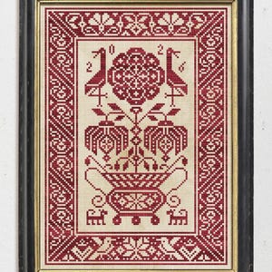May include: A framed cross-stitch embroidery featuring a deep red geometric pattern on a light beige fabric. The design displays a central floral motif in a decorative urn, flanked by two birds and the year 2016, all enclosed in a border.
