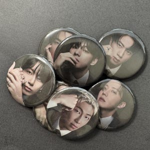 May include: A collection of six round pinback buttons featuring portraits of various individuals. The buttons have a glossy finish and are arranged in a slightly overlapping pattern. The portraits are in shades of gray and black.
