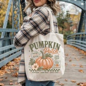 May include: A cream-colored canvas tote bag featuring a graphic print of a large orange pumpkin with green leaves and flowers. The text reads PUMPKIN Patch, FRESH FROM THE PATCH, FARM FRESH, LOCALLY GROWN, AUTUMN PICKED, PUMPKINS, CORN MAZE, APPLE CIDER.
