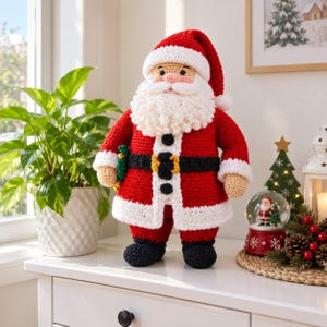 May include: A crocheted Santa Claus doll featuring a red coat with white trim, a black belt with a yellow buckle, a thick white beard, and a matching red hat. The doll has tan skin, black eyes, and black boots, standing upright as a decorative figure.