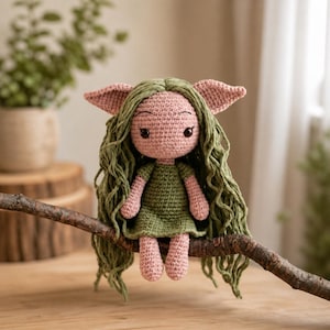 May include: A handmade crochet doll with a pink face, ears, and hands, and a green dress and hair. The doll is sitting on a brown branch. The doll has large eyes and is made of yarn.