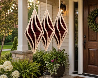 May include: Three diamond-shaped hanging ornaments featuring a deep burgundy centre and a thick, cream-coloured crocheted border. Each ornament is suspended by a matching cream-coloured string, creating a vertical display of geometric decor.