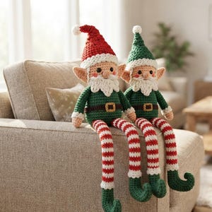 May include: Two handmade crochet elf dolls with long legs. One elf wears a red hat, the other a green hat. Both have white beards, green shirts, brown belts with gold buckles, and red and white striped legs with curled green feet.
