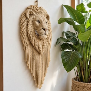 Puede incluir: Una escultura de pared con forma de cabeza de león hecha de cuerda beige. El diseño presenta un rostro detallado con una melena gruesa y texturizada hecha de hebras de cuerda verticales que se extienden hacia abajo en un largo fleco.