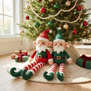 May include: Two handmade crochet elf dolls with pointed hats, white beards, and long striped legs. One elf wears a red hat and green shirt, while the other wears a green hat and red shirt. Both dolls feature brown belts with gold buckles.