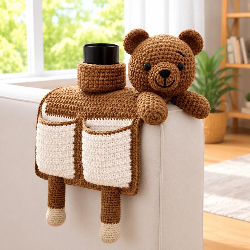 Puede incluir: Organizador de brazo de sof&aacute; tejido a ganchillo en marr&oacute;n y blanco con dise&ntilde;o de oso de peluche. Cuenta con dos bolsillos blancos, un portavasos y dos patas colgantes. El oso de peluche est&aacute; en el brazo del sof&aacute;.
