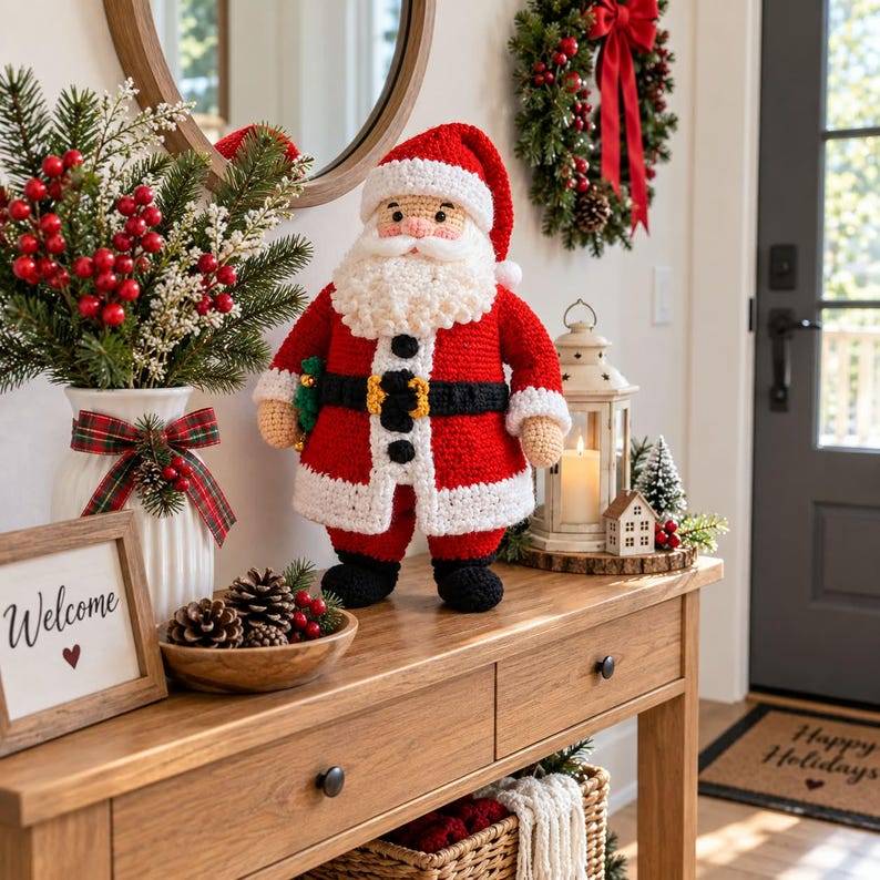 May include: A crocheted Santa Claus figurine featuring a red coat, white trim, a black belt with a yellow buckle, and black boots. The Santa has a white beard and a red hat. It stands on a wooden console table next to a white vase with red berries.