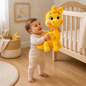 May include: A smiling baby holds a large, yellow crocheted dinosaur toy with orange spots. The dinosaur has a bow on its head and rosy cheeks. A crib, a basket with a teddy bear and star-shaped pillow, and a framed picture of a moon and clouds are in the background.