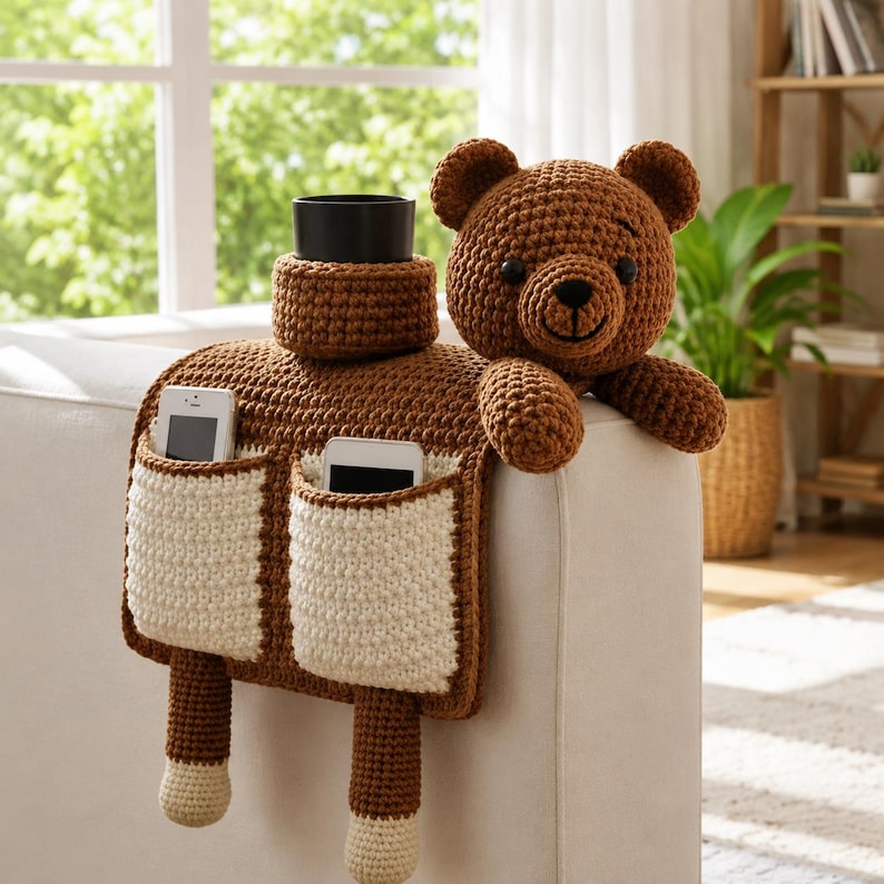 Puede incluir: Un organizador de brazo de sof&aacute; tejido a ganchillo marr&oacute;n y crema con un dise&ntilde;o de oso de peluche. Cuenta con dos bolsillos para tel&eacute;fonos, un portavasos y una cabeza de oso de peluche. La cabeza del oso es marr&oacute;n con nariz y ojos negros.