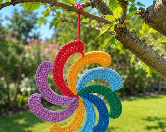May include: A multi-coloured crochet ornament featuring a spiral design with six curved segments in red, orange, light blue, green, dark blue, and purple. The ornament is suspended by a matching red crocheted loop attached to the top centre.