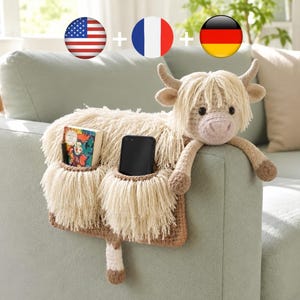 May include: A plush, Highland cow-shaped couch organizer in cream and brown. It features two pockets for storage, one holding a book and the other a smartphone. The cow's head and arms drape over the couch arm, adding a decorative touch.