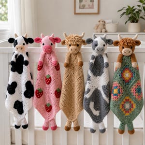 May include: Five crocheted animal security blankets featuring cow and highland cattle heads. The blankets include a black and white cow, a pink strawberry-patterned cow, a tan highland cow, a grey and white cow, and a multi-colored granny square cow.