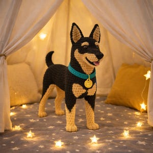 Könnte beinhalten: Gehäkelte Hundefigur in Schwarz und Beige, mit türkisfarbenem Halsband und goldenem Anhänger. Der Hund befindet sich in einem Zelt mit Sternlichtern und Kissen. Die Zunge des Hundes ist sichtbar. Ungefähr 30 cm hoch.