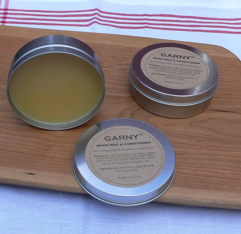 May include: Two silver tins of wood wax and conditioner, labeled "GARNY&trade; WOOD WAX & CONDITIONER". The label on the tin on the left says "For Cutting Boards, Finished or Raw Wood. Direction: Use it on clean dry wood. Apply small amount on a soft cloth (old T-shirt works fine) and rub on the surface. Wait about 30 minutes and buff it off. Ingredients: Walnut Oil, Bees Wax & Carnauba Wax. Made in U.S.A."