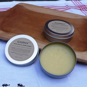 May include: Two silver tins of wood wax and conditioner, labeled "GARNY&trade; WOOD WAX & CONDITIONER" with instructions for use and ingredients. The tins are on a wooden surface.