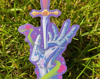 May include: A sticker featuring a stylized illustration of a hand in silver armor holding a sword. The sword has a pink and gold handle and a silver blade. The hand is set against a purple background with green vines and pink roses.