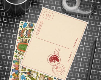 May include: A cream-coloured postcard featuring a red stamp graphic with a panther and a peach, along with the text Atlanta, Georgia. The postcard includes a stamp box and address lines, displayed alongside a black mug, tape dispenser, and pencil.