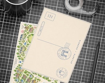 May include: A cream-coloured postcard featuring a map of the Clark Atlanta University campus with illustrations of buildings and trees, alongside a blank postcard back with Atlanta, Georgia postmark stamps, a black mug, tape dispenser, and a black pencil.