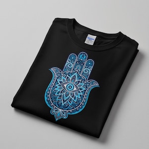 May include: Black crew neck t-shirt featuring a detailed blue Hamsa hand design. The Hamsa hand, with an eye in the center, is a symbol of protection. The design is intricate with floral and geometric patterns, creating a striking contrast against the black fabric.