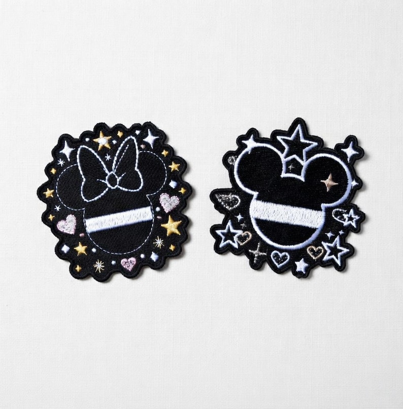 Puede incluir: Dos parches bordados en blanco y negro con un dise&ntilde;o de cabeza de rat&oacute;n. Uno tiene un lazo, el otro estrellas y corazones. Ambos tienen una franja blanca y est&aacute;n rodeados de estrellas y corazones.