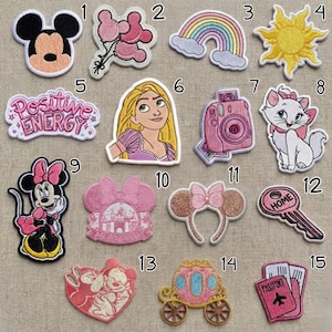 Op de afbeelding: Collectie geborduurde patches met diverse ontwerpen. Inclusief Mickey Mouse, Minnie Mouse, een regenboog, een zon, een camera, een kat, Rapunzel, een sleutel met "HOME", een koets en paspoort patches. De patches zijn in verschillende kleuren.