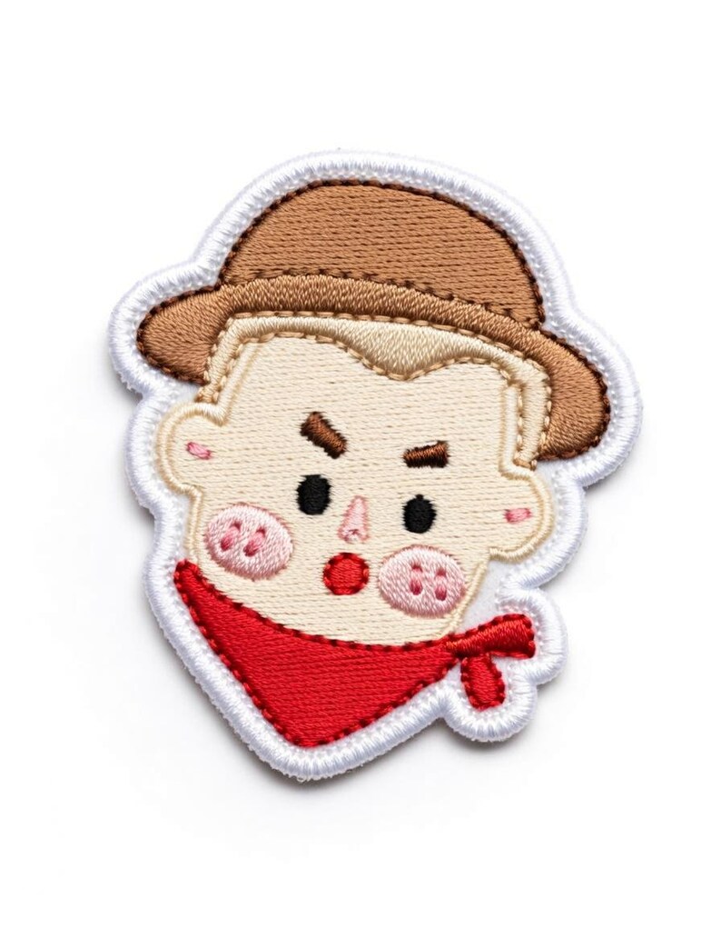 Puede incluir: Parche bordado con la cara de un vaquero de dibujos animados. El dise&ntilde;o incluye un sombrero marr&oacute;n, un pa&ntilde;uelo rojo y mejillas rosadas. El parche est&aacute; contorneado con costuras blancas.