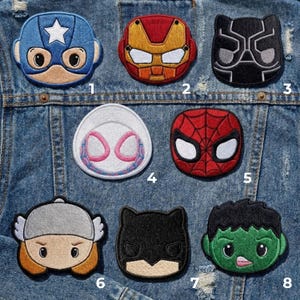 May include: A collection of eight embroidered patches featuring superhero characters. The patches include Captain America, Iron Man, Black Panther, Spider-Man, Spider-Gwen, Thor, Batman, and the Hulk. The patches are in various colors and designs.