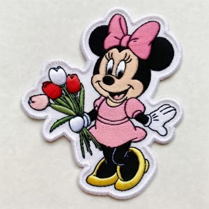 Op de afbeelding: Geborduurde patch met een cartoon muis karakter in een roze jurk en strik, met een boeket tulpen. De patch heeft een witte rand en is geschikt voor toepassing op kleding of accessoires.