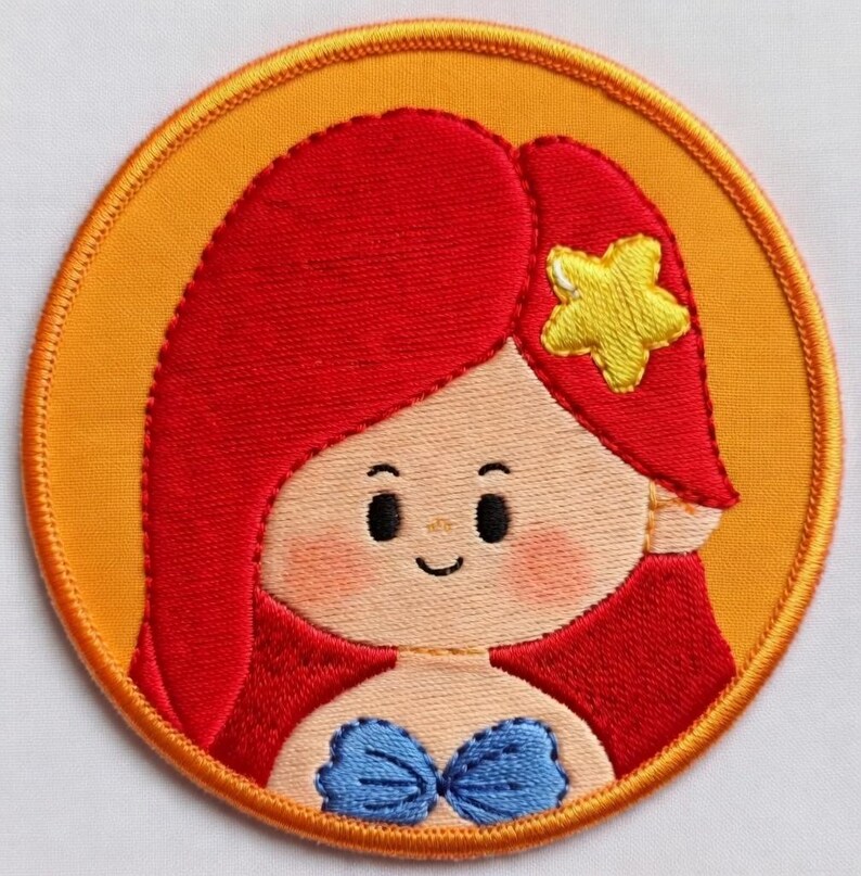 May include: Embroidered patch of a cartoon mermaid with red hair, a yellow starfish, and a blue seashell top. The round patch has an orange background and a yellow border.