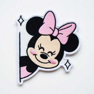 Op de afbeelding: Geborduurde patch met een lachende cartoonmuis met een roze strik en roze wangen. De muis is zwart en bruin met een witte rand en twee fonkelende diamantvormen. De patch is ontworpen om eruit te zien alsof de muis achter een wit oppervlak vandaan gluurt.