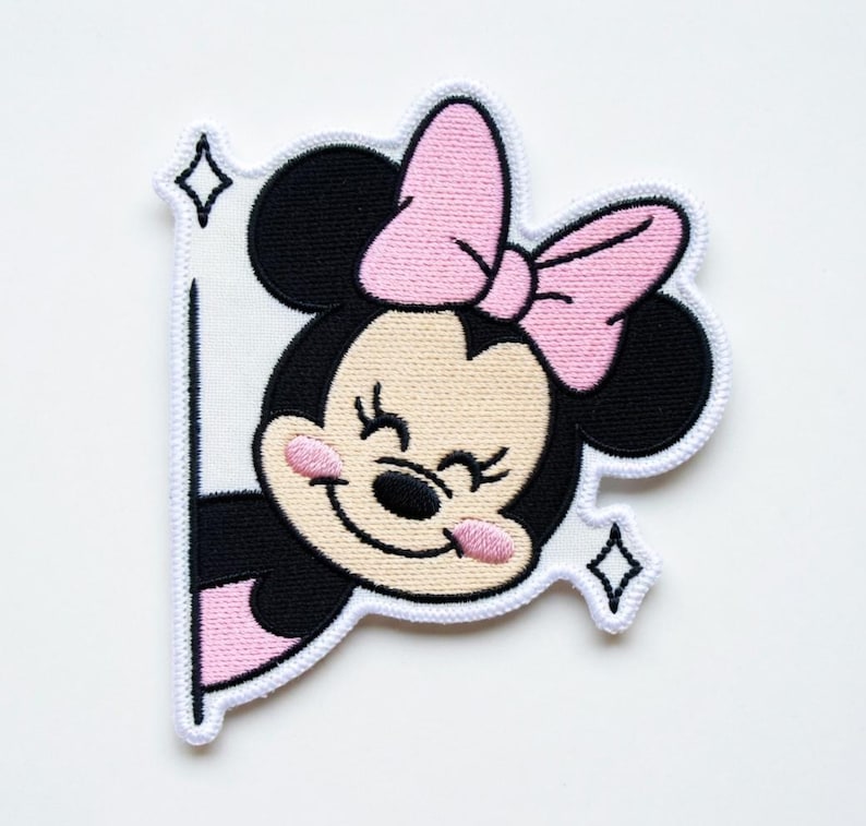 Op de afbeelding: Geborduurde patch met een lachende cartoonmuis met een roze strik en roze wangen. De muis is zwart en bruin met een witte rand en twee fonkelende diamantvormen. De patch is ontworpen om eruit te zien alsof de muis achter een wit oppervlak vandaan gluurt.
