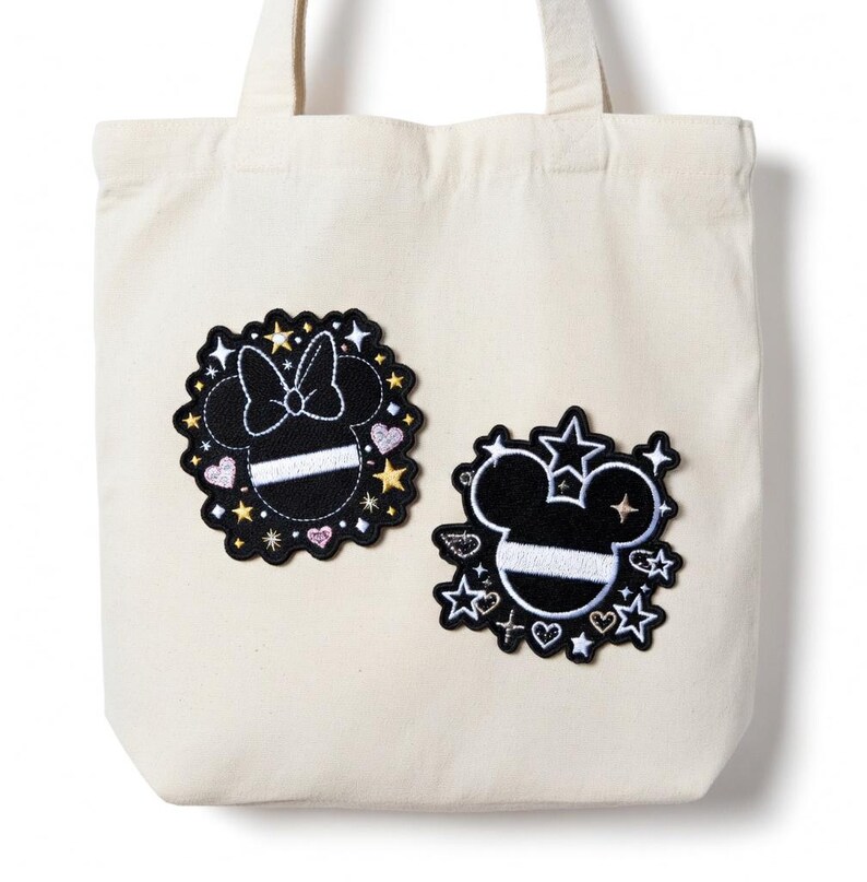 Puede incluir: Bolso tote color crema con dos parches de Mickey Mouse en blanco y negro. Un parche presenta un lazo, el otro tiene estrellas y una estrella fugaz. Ambos parches tienen una franja blanca y est&aacute;n rodeados de estrellas y corazones.