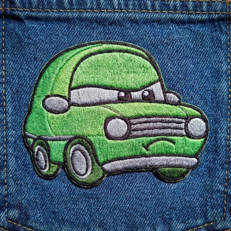 Puede incluir: Un parche de coche bordado verde con un dise&ntilde;o de dibujos animados, con una cara sonriente y ruedas grandes. El parche est&aacute; cosido sobre una tela vaquera azul, mostrando los detalles de los faros, la parrilla y las ventanas del coche.