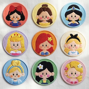 May include: Nine embroidered patches featuring cartoon illustrations of princesses. Each patch is round with a coloured border and depicts a different princess with unique hairstyles and outfits. The patches are colourful and detailed.