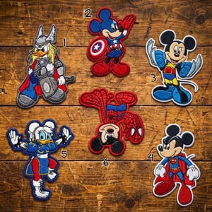May include: A collection of six colorful embroidered patches featuring cartoon characters in superhero costumes. The patches include Thor, Captain America, Wolverine, Superman, and Spider-Man, with a Daisy Duck as Chun-Li.