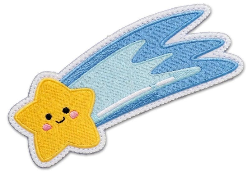 Puede incluir: Parche bordado con una estrella amarilla sonriente con mejillas rosadas, que sigue un cometa azul. El cometa tiene detalles en azul claro y blanco, todo delineado con costuras blancas. Un dise&ntilde;o lindo y caprichoso.