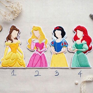 May include: Four embroidered patches featuring cartoon princesses in colorful gowns. Belle in yellow, Aurora in pink, Snow White in blue and yellow, and Ariel in green. Each patch has a white border and a number below.