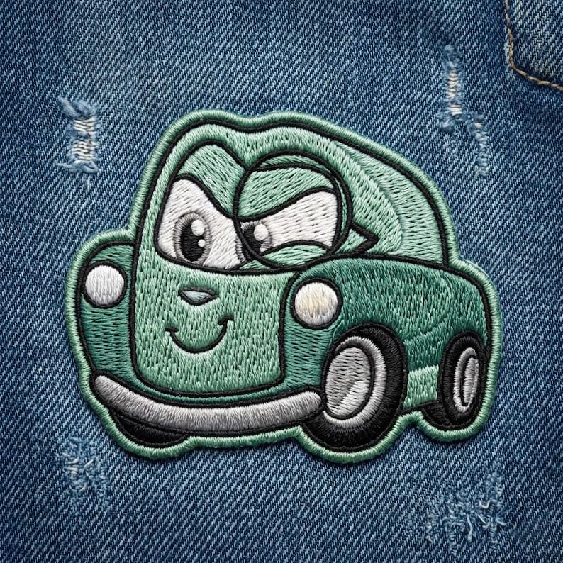 Puede incluir: Parche bordado de un coche de dibujos animados verde sonriente, con ojos grandes. El parche tiene contornos negros y est&aacute; sobre un fondo de mezclilla azul. El coche tiene dos faros y dos ruedas.