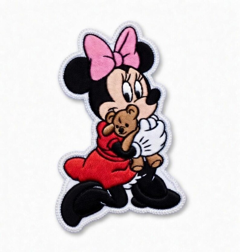 Op de afbeelding: Geborduurde patch met een stripfiguur met een roze strik, zwarte oren en een rode jurk, die een kleine bruine teddybeer vasthoudt. Het personage heeft witte handschoenen en zwarte schoenen, met een witte rand.