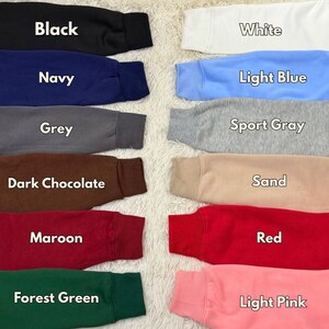 May include: A collection of sweatshirt sleeves in various colors, including black, navy, grey, dark chocolate, maroon, forest green, white, light blue, sport gray, sand, red, and light pink. Each sleeve has a ribbed cuff and is labeled with its color name.