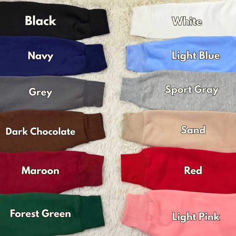 May include: A collection of sweatshirt sleeves in various colors, including black, navy, grey, dark chocolate, maroon, forest green, white, light blue, sport gray, sand, red, and light pink. Each sleeve has a ribbed cuff and is labeled with its color name.