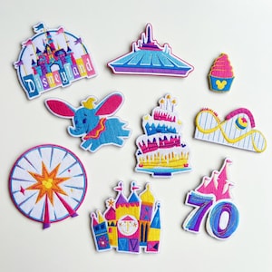 May include: A collection of colorful embroidered patches featuring iconic Disneyland imagery. Includes a castle, Space Mountain, Dumbo the flying elephant, a Ferris wheel, a birthday cake, a roller coaster, a cupcake, a castle, and a "70" patch.