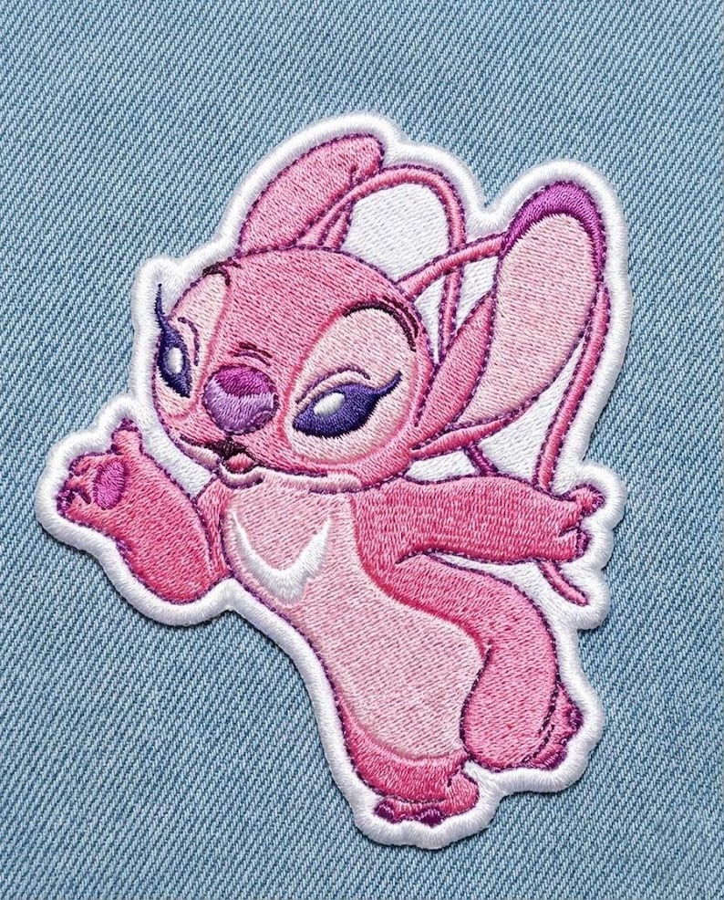 Puede incluir: Parche bordado rosa con el personaje Angel de la pel&iacute;cula Lilo & Stitch. El parche tiene un borde blanco y est&aacute; sobre un fondo de mezclilla azul claro. Angel se representa con orejas grandes, ojos morados y una pose acogedora.