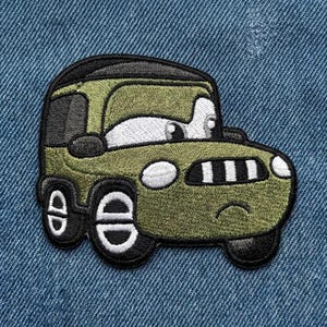 Puede incluir: Un parche bordado con un coche de dibujos animados en verde oliva, negro y blanco. El coche tiene ojos grandes y una boca sonriente. El parche est&aacute; dise&ntilde;ado para planchar o coser sobre ropa o telas.
