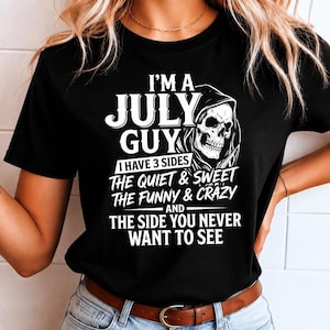 May include: A black short-sleeved t-shirt featuring white text that reads I'M A JULY GUY I HAVE 3 SIDES THE QUIET & SWEET THE FUNNY & CRAZY AND THE SIDE YOU NEVER WANT TO SEE, accompanied by a graphic illustration of a hooded skull.